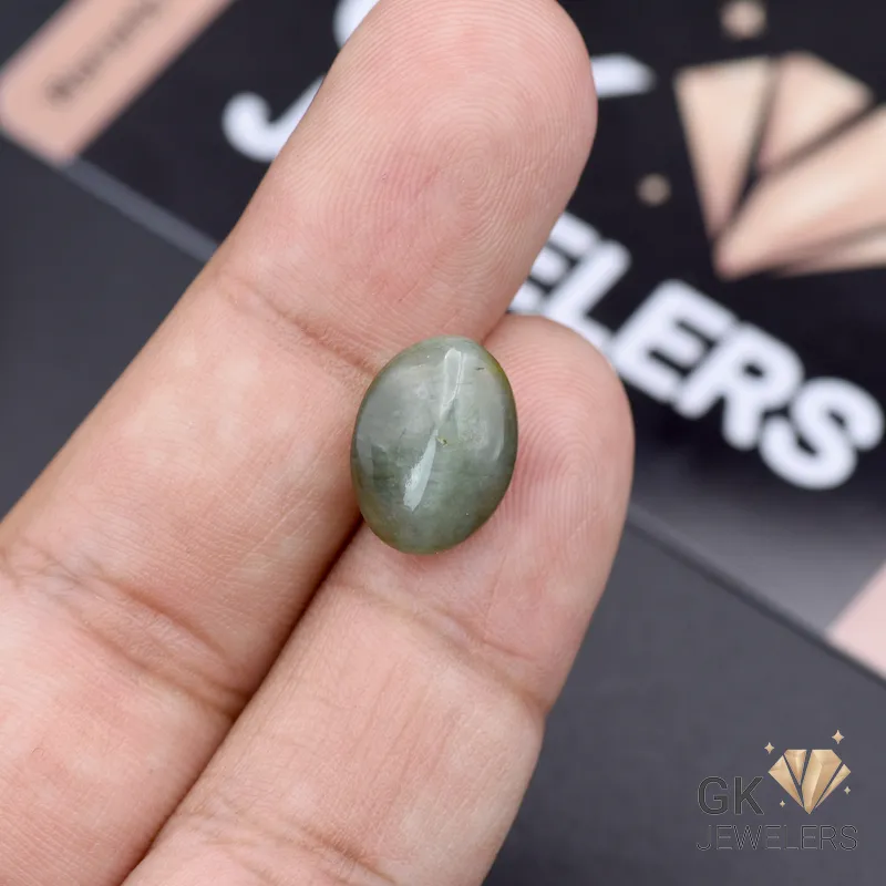 Oval-cut green catseye gemstone held between fingers, showcasing its opaque transparency and silky luster