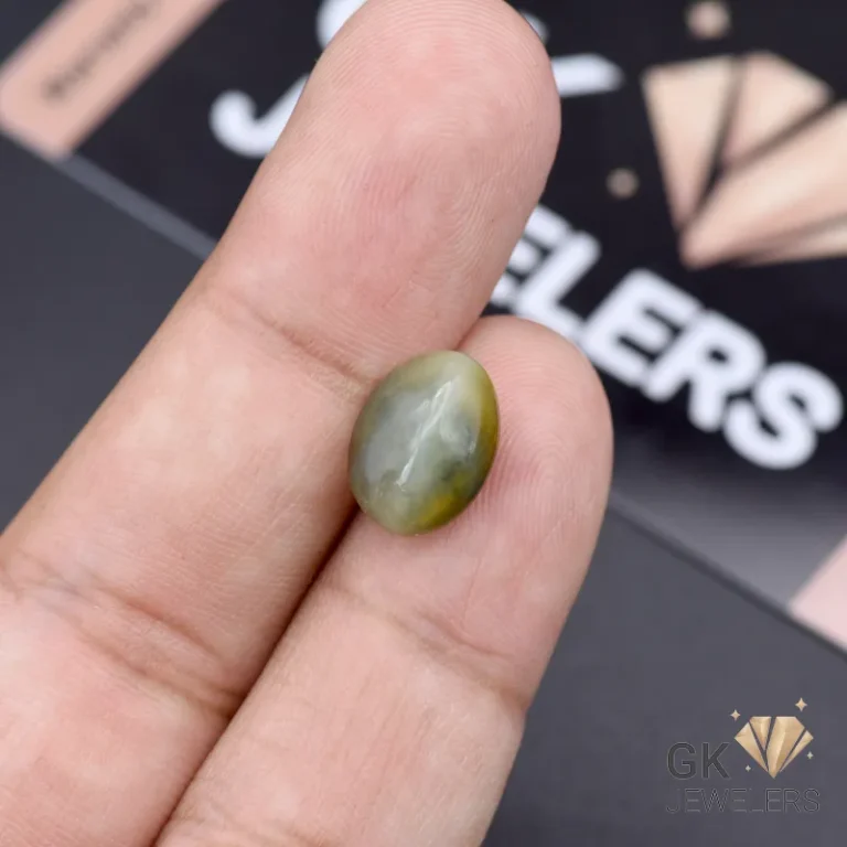 Oval-shaped green catseye gemstone with chatoyancy held between fingers, showcasing opaque transparency