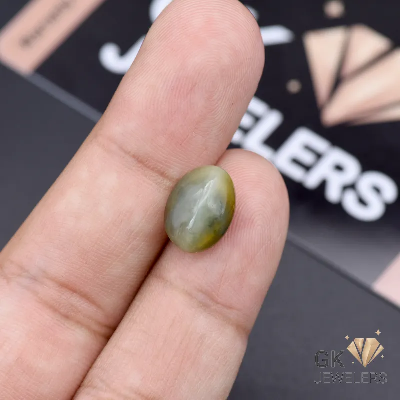 Oval-shaped green catseye gemstone with chatoyancy held between fingers, showcasing opaque transparency