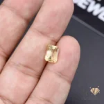 Emerald-cut citrine gemstone held between fingers, showcasing transparent yellow color and brilliant facets