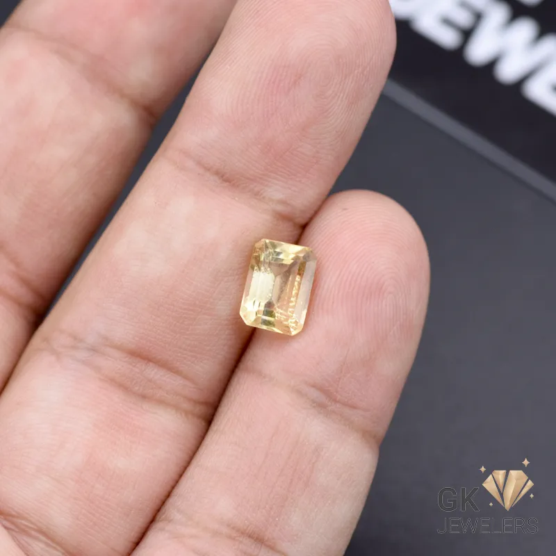 Emerald-cut citrine gemstone held between fingers, showcasing transparent yellow color and brilliant facets