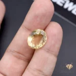 Oval-cut citrine gemstone weighing 11.65 carats held between fingers, showcasing transparent yellow color