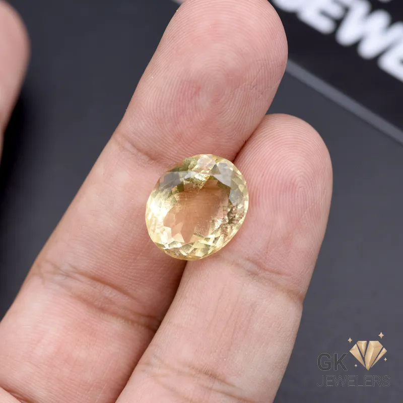 Oval-cut citrine gemstone weighing 11.65 carats held between fingers, showcasing transparent yellow color