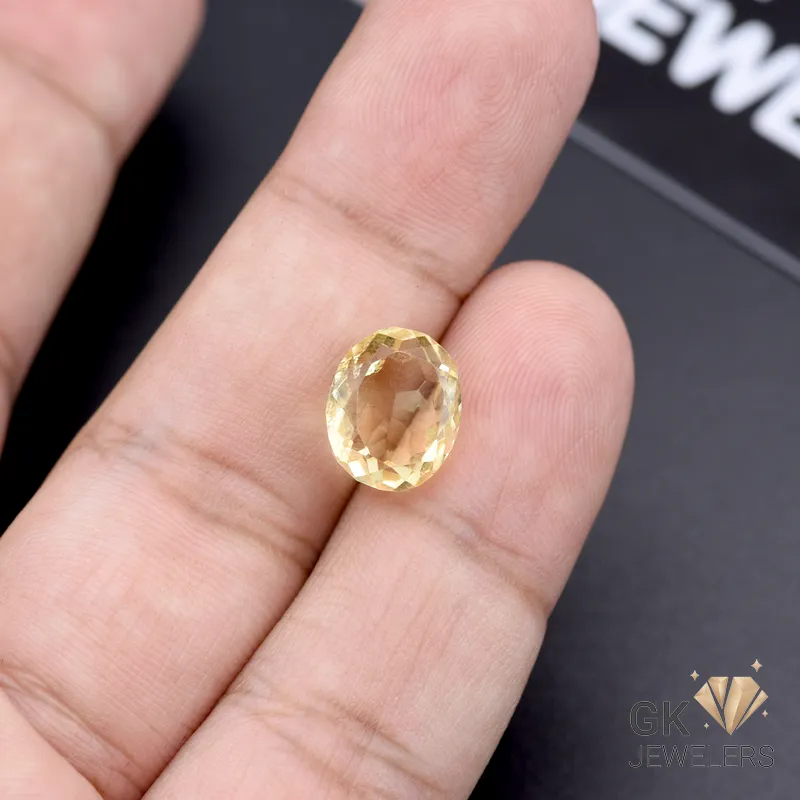 Oval-cut yellow citrine gemstone held between fingers, showcasing transparent clarity and golden tones