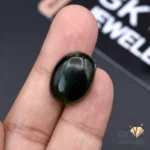 Dark green oval-cut jade gemstone held between fingers, showcasing translucent quality
