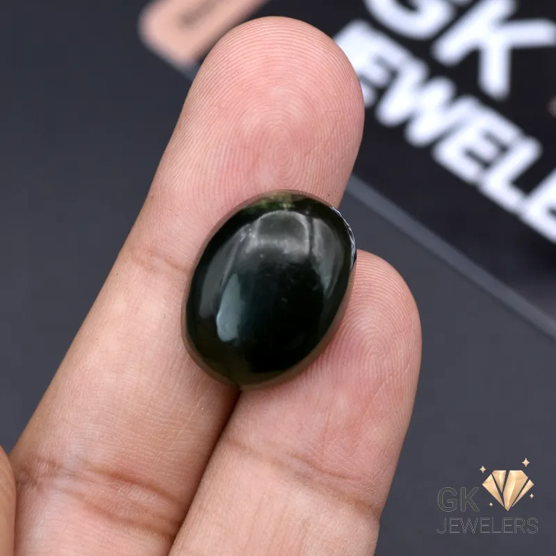 Dark green oval-cut jade gemstone held between fingers, showcasing translucent quality