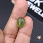 Hand holding a 5.35-carat oval-cut natural jade gemstone with semi-transparent green color