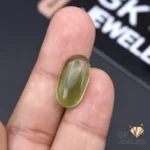 Hand holding an oval-cut semi-transparent green jade gemstone against a dark background with GK Jewelers logo