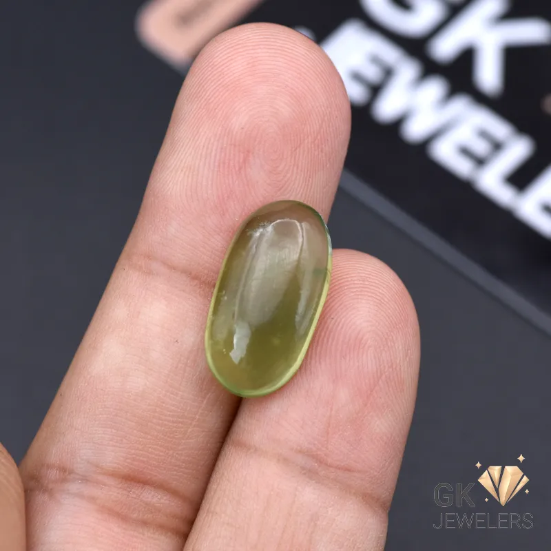 Hand holding an oval-cut semi-transparent green jade gemstone against a dark background with GK Jewelers logo