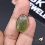 Oval-shaped, semi-transparent green jade gemstone held between fingers, showcasing its natural luster and Russian origin