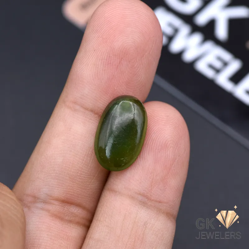 Oval-shaped natural jade gemstone held between fingers, showcasing semi-transparent green color