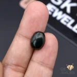 Dark green natural jade stone held between fingers, showcasing its translucent properties and round cut