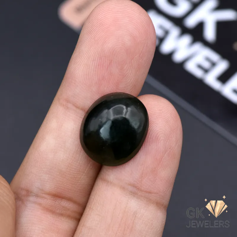 Hand holding a dark green, translucent, 11.60-carat jade gemstone with a smooth, round surface, against a blurred 'GK JEWELERS' background