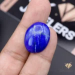 Hand holding a 21.05-carat oval-cut natural Lapis Lazuli gemstone with deep blue color and white speckles