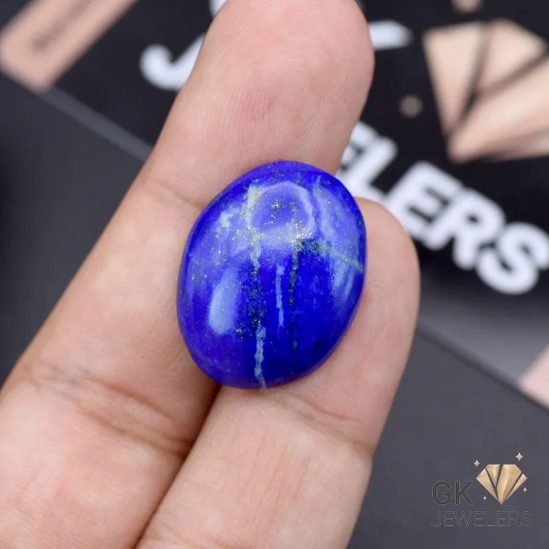 Hand holding a 21.05-carat oval-cut natural Lapis Lazuli gemstone with deep blue color and white speckles