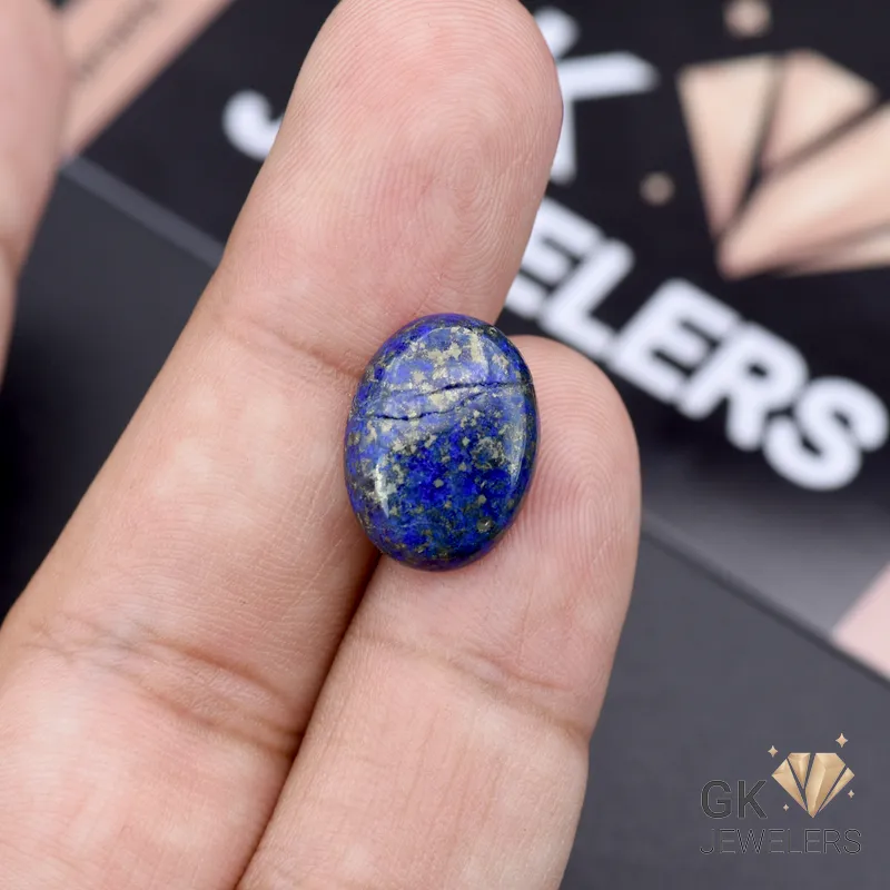 Oval-cut lapis lazuli gemstone held between fingers, displaying rich blue color with gold flecks