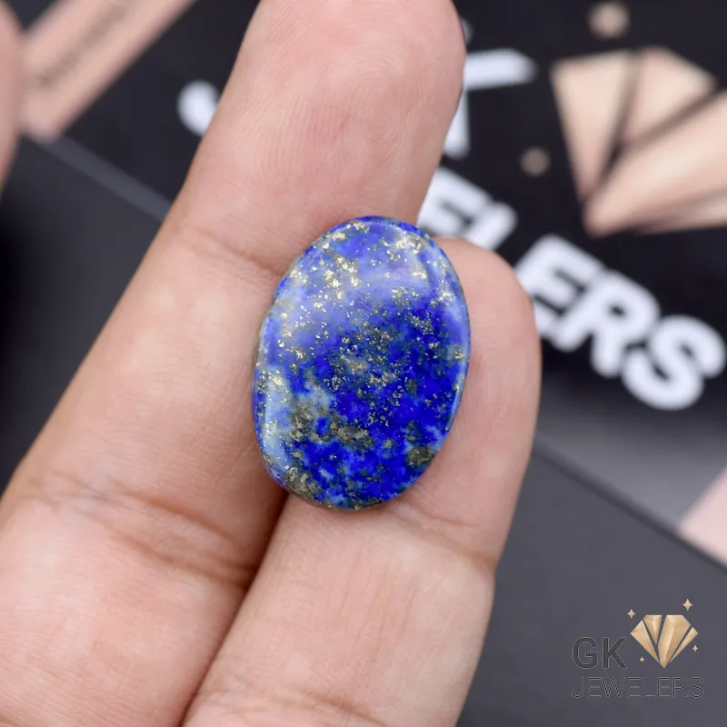 Hand holding an oval-shaped lapislazuli gemstone with gold flecks against a dark background