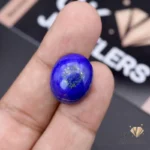 Hand holding a round, opaque blue lapislazuli gemstone with gold flecks, weighing 23.75 carats from Afghanistan