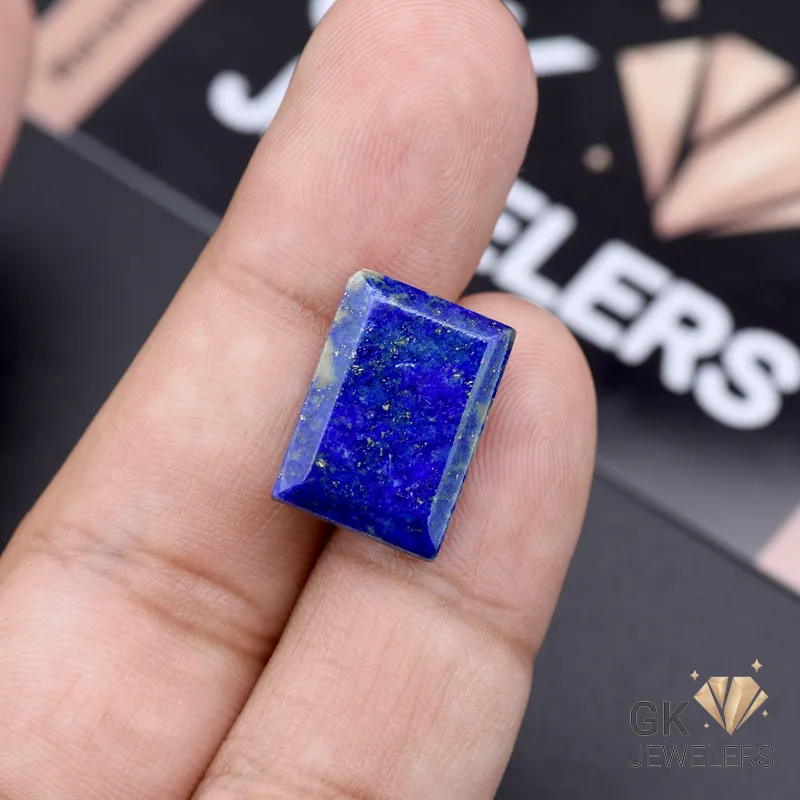 Emerald-cut lapis lazuli gemstone held between fingers, showcasing deep blue color with gold flecks