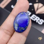 Oval-shaped lapis lazuli gemstone with gold flecks held between fingers