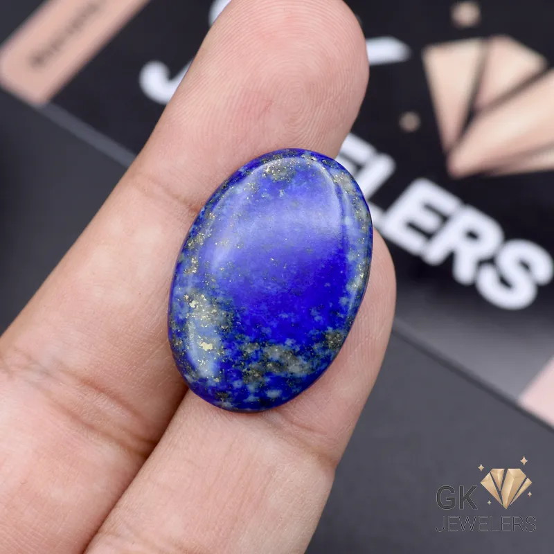 Oval-shaped lapis lazuli gemstone with gold flecks held between fingers