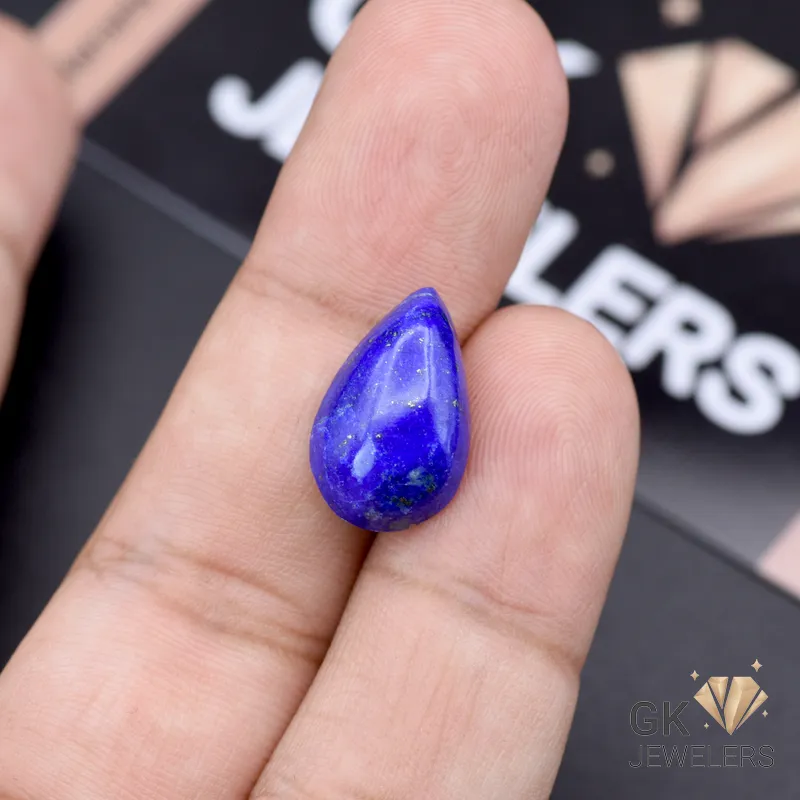 Hand holding a teardrop-shaped lapis lazuli gemstone with deep blue color and golden specks