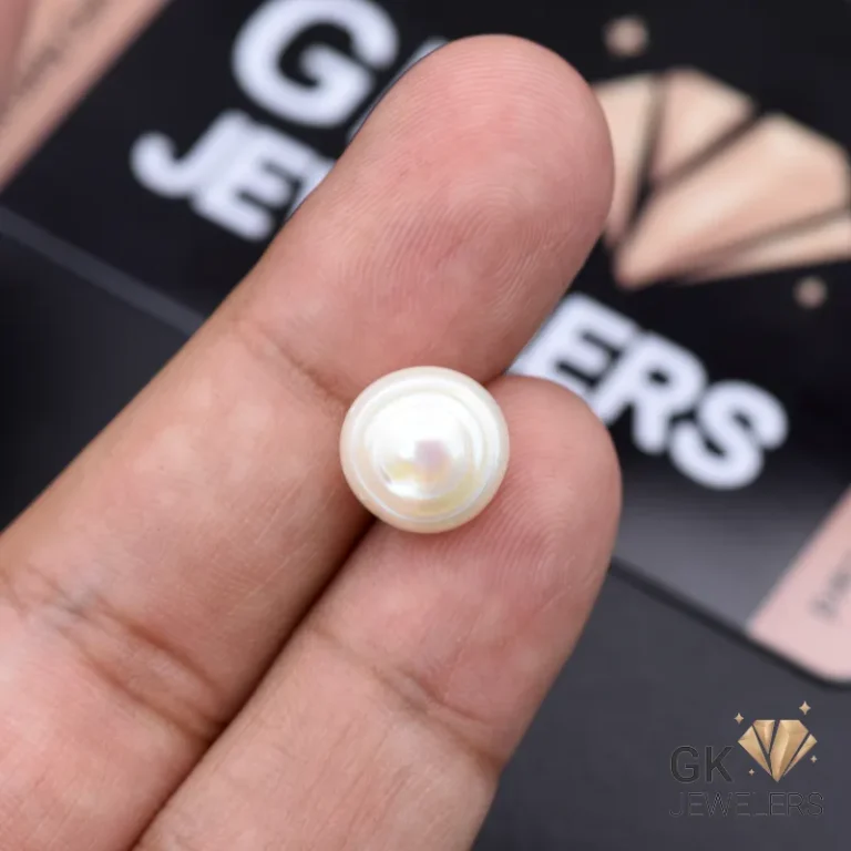 White natural pearl gemstone held between fingers against a blurred jewelry advertisement background