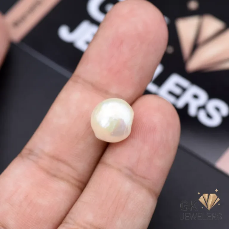 Hand holding a 7.40ct white natural pearl gemstone from Africa, showcasing its opaque pearlescent glow