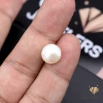 Hand holding a 7.20-carat white natural pearl between thumb and index finger