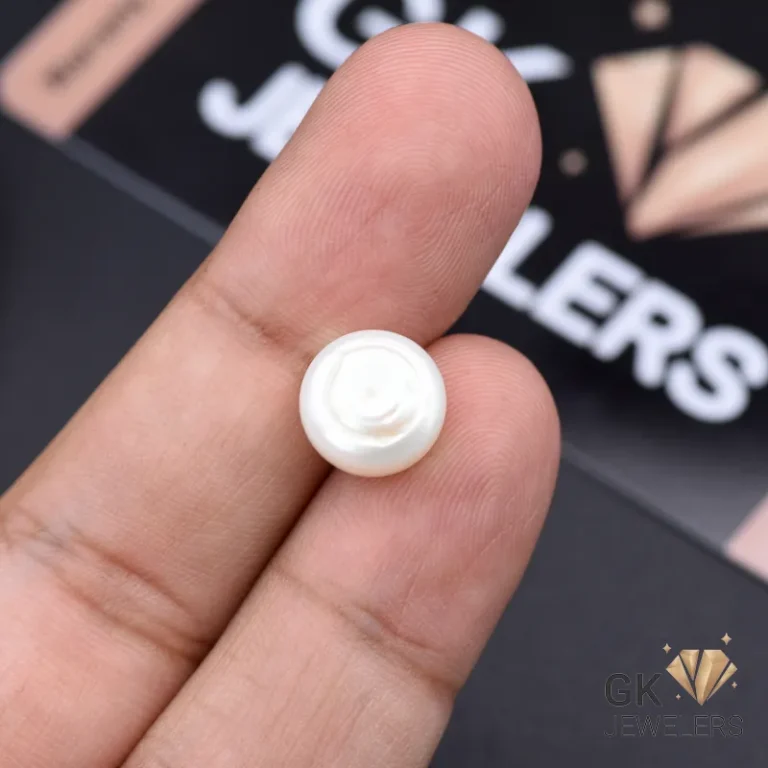 White natural pearl gemstone held between fingers, showcasing its round shape and opaque quality