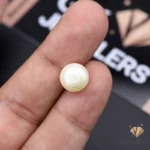 White 6.80-carat natural pearl held between fingers, showcasing its round shape and opaque quality