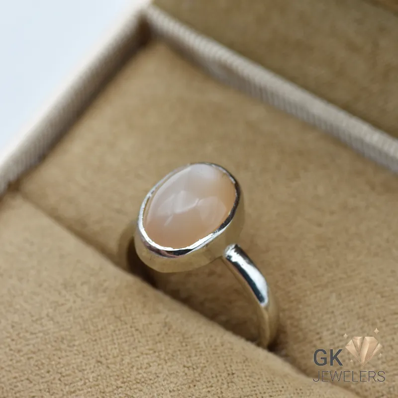 Oval pink moonstone cabochon set in handmade silver ring, displayed in a jewelry box with beige fabric lining