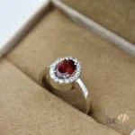 Oval-cut red garnet gemstone ring with diamond halo in silver band, handmade setting