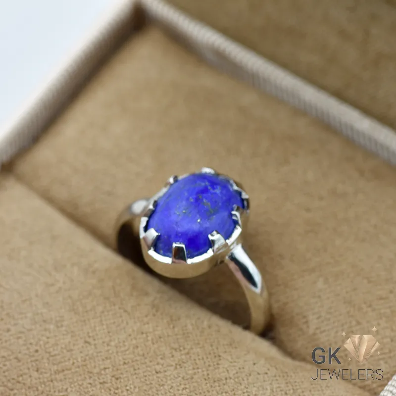 Oval-cut natural Lapis Lazuli gemstone set in handmade silver ring, displayed on beige jewelry box fabric, showcasing deep blue color