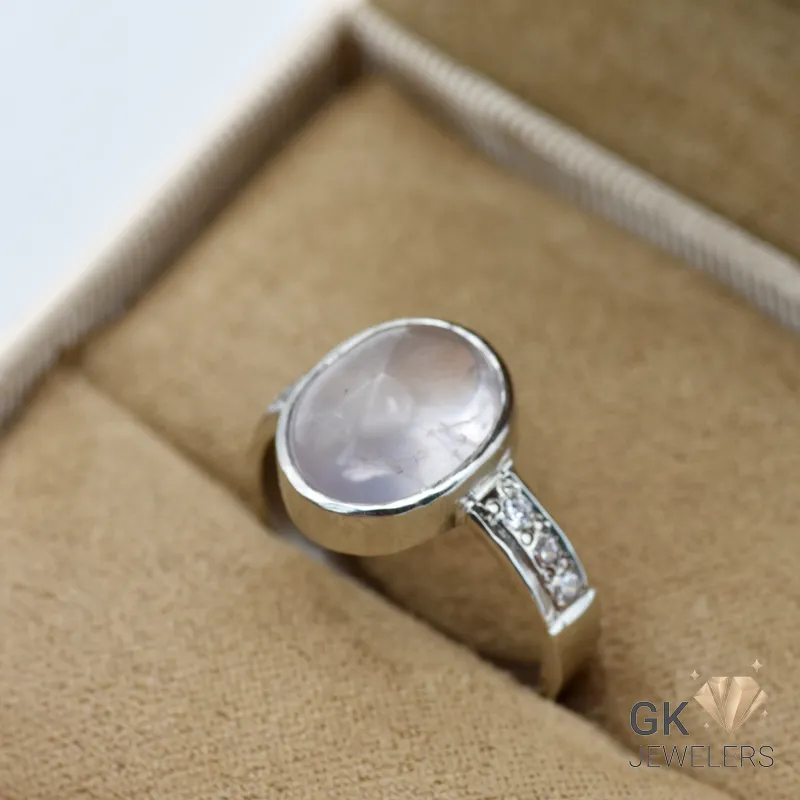 Oval rose quartz gemstone set in handmade silver ring with diamond details on band, displayed in a jewelry box
