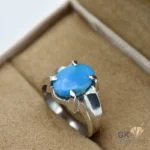 Oval blue turquoise gemstone set in a sterling silver ring with six prongs, displayed on a beige jewelry box insert