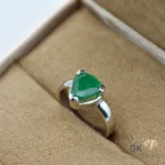 Heart-shaped emerald gemstone set in silver ring with handmade setting, showcasing translucent green clarity