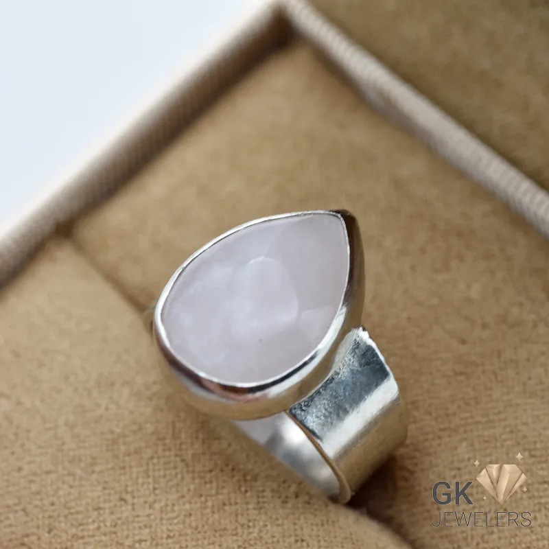 Pear-shaped rose quartz gemstone set in sterling silver ring, displayed on tan fabric in a jewelry box