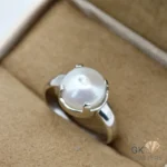 Round white pearl set in sterling silver four-claw setting, displayed in a beige jewelry box with a soft fabric interior