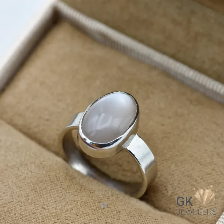 Oval gray moonstone set in sterling silver ring, displayed in beige jewelry box with textured interior