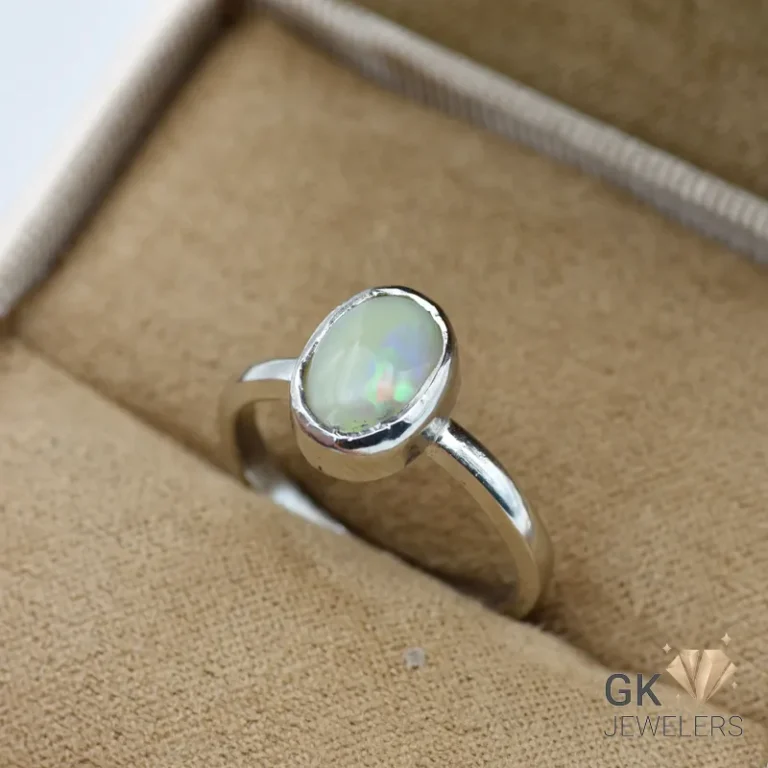 Oval-shaped white opal gemstone set in a handmade silver ring, showcasing iridescent colors, on a beige jewelry box fabric