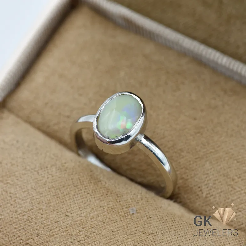 Oval-shaped white opal gemstone set in a handmade silver ring, showcasing iridescent colors, on a beige jewelry box fabric