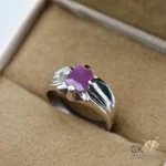 Silver ring featuring an emerald-cut ruby gemstone with pinkish red color, set in handmade silver craftsmanship, displayed on beige fabric