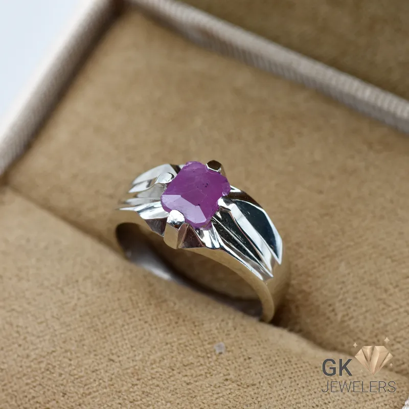 Silver ring featuring an emerald-cut ruby gemstone with pinkish red color, set in handmade silver craftsmanship, displayed on beige fabric