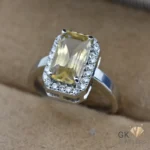 Silver ring featuring a large, transparent yellow citrine gemstone in an emerald cut setting, surrounded by smaller white gemstones