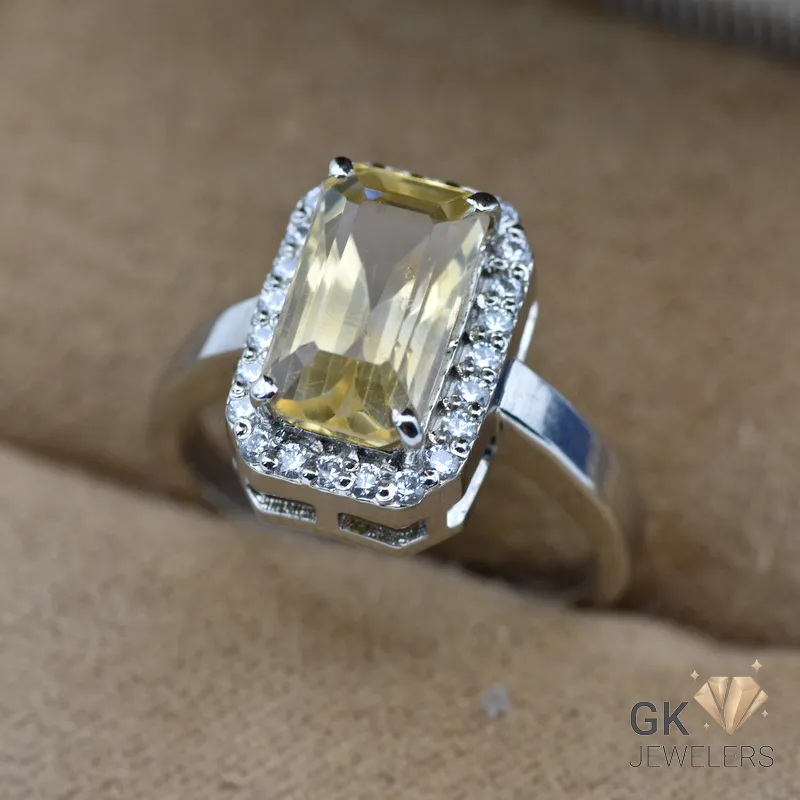Silver ring featuring a large, transparent yellow citrine gemstone in an emerald cut setting, surrounded by smaller white gemstones