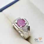 Purplish red ruby gemstone set in handmade silver ring with diamond accents on a white jewelry box cushion