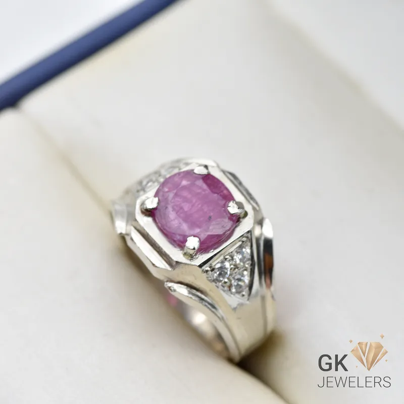 Purplish red ruby gemstone set in handmade silver ring with diamond accents on a white jewelry box cushion