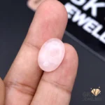 Oval-cut rose quartz gemstone held between fingers, displaying translucent pink hue and exceptional clarity