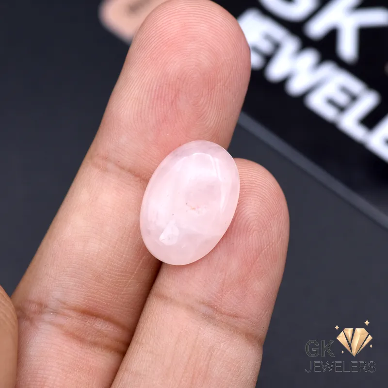 Oval-cut rose quartz gemstone held between fingers, displaying translucent pink hue and exceptional clarity
